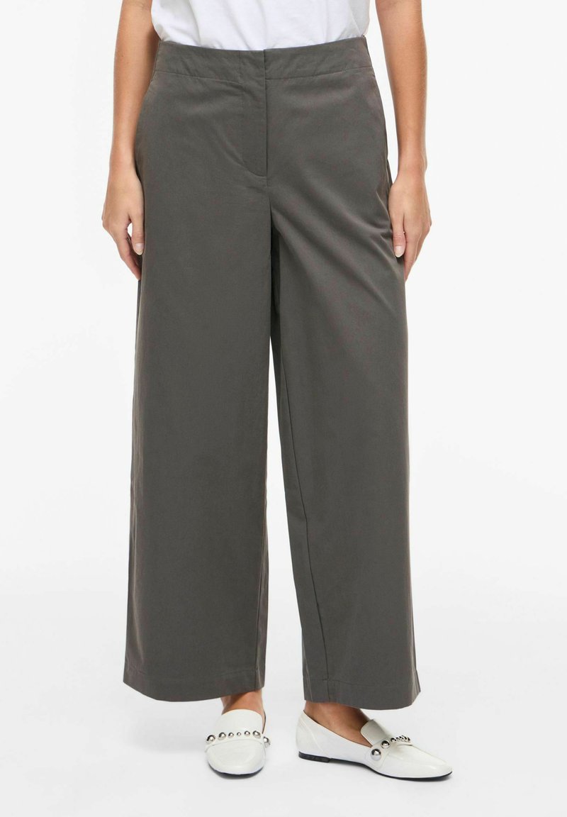 Platus tamsiai pilkos spalvos audinio sijonas, pasižymintis lygiu tekstūru ir plokščiu priekiu. Derinamos su baltais slip-on batais.