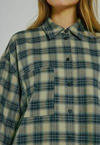 Oversized rutig skjorta i beige med blå och svarta toner. Knäppning fram, traditionell krage och textil med struktur.