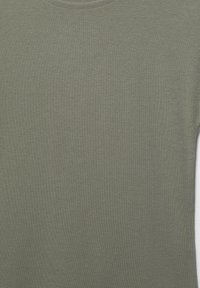 Gros plan d’un t-shirt en coton uni vert olive à manches courtes, montrant la texture du tissu et l’ourlet supérieur.
