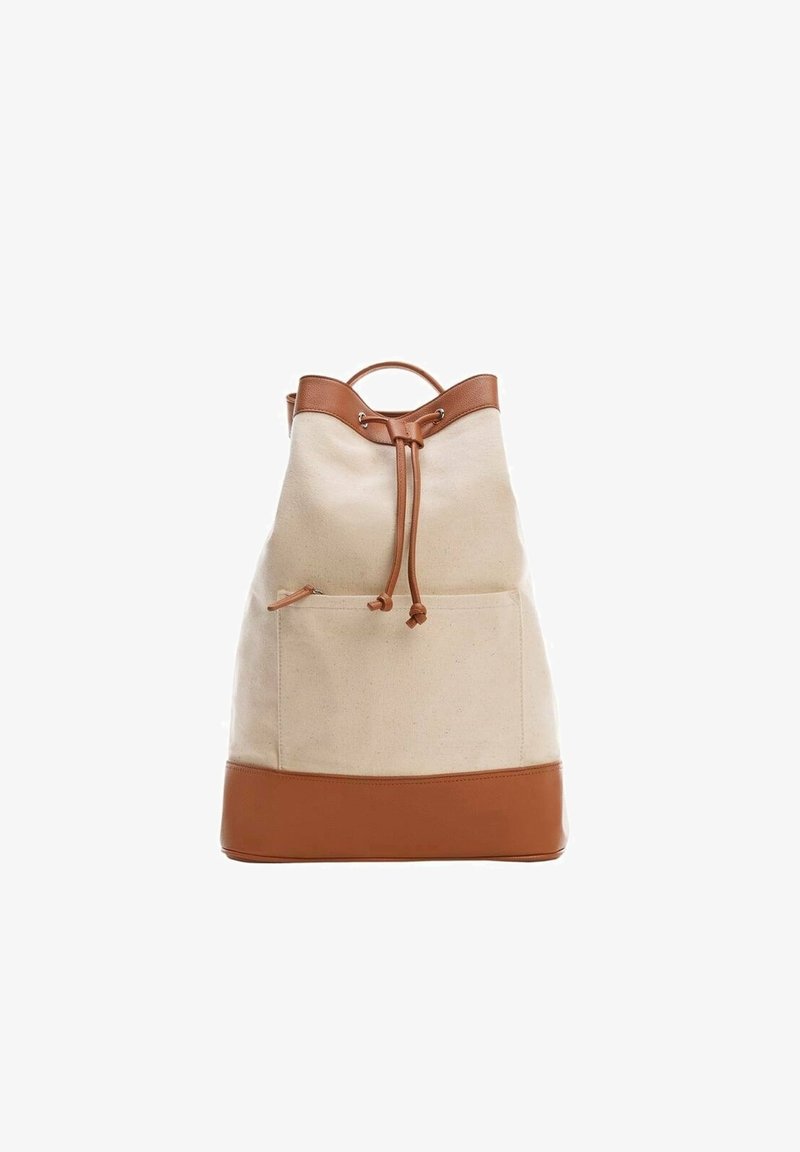 Sac à dos en toile beige avec garniture en cuir marron, fermeture par cordon, poche avant et poignée supérieure sur fond blanc.