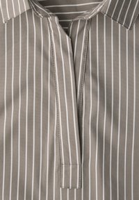 Chemise beige à fines rayures verticales blanches, avec un col et une patte de boutonnage partielle au centre devant.