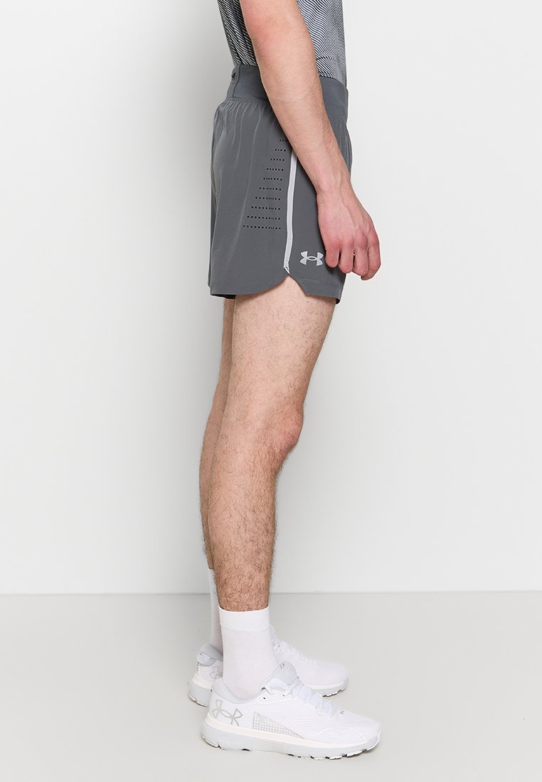 Pantaloni sportivi grigi con lati perforati e cintura elastica, abbinati a scarpe e calze sportive bianche, visti di lato.