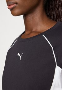 Zwarte sportshirt met witte accenten, voorzien van een ronde halslijn en een klein wit Puma-logo op de borst. Glad katoenmateriaal.