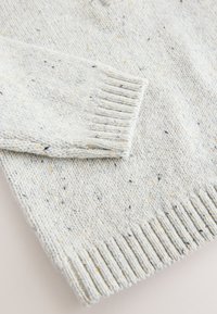 Lys grå strikket sweater med tekstureret finish, der har små pletter i blå, gul og sort. Ribstrikkede manchetter og kantdetaljer.