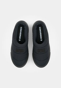 Sorte polstrede slip-on sko med gummisåler, der har en tekstureret stofoverdel og prægede logo-detaljer på siden.