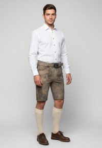 Tradycyjny strój składający się z białej koszuli i beżowych lederhosen z ozdobnym haftem. Dodatki to czarny pasek i skarpetki do kolan.