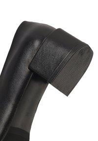 Chaussure à talon haut en cuir noir avec un bout carré et un talon épais. Le talon présente une surface texturée avec un fond plat et un branding subtil.