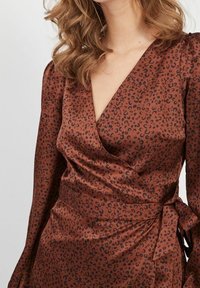 Vestido de satén marrón con estampado de leopardo negro, diseño envolvente, escote en forma de V, mangas largas y detalle de lazo lateral para un ajuste ceñido.
