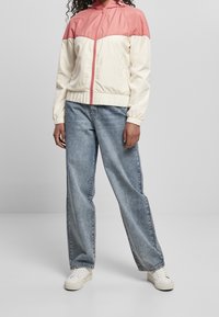 Lekka wiatrówka w kolorze kremowym i różowym z zamkiem, elastycznymi mankietami i dołem. W połączeniu z luźnymi dżinsami i białymi trampkami.