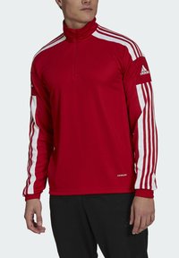 Red long-sleeve athletic top with a quarter zip, white three-stripe design on sleeves, made from moisture-wicking fabric, featuring "AEROREADY" branding.