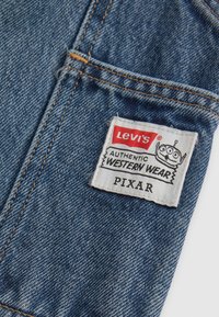 Tela de denim con tonos azules, que presenta una etiqueta blanca con texto rojo. La etiqueta dice "Levi's Authentic Western Wear" e incluye un gráfico de un personaje de Pixar.