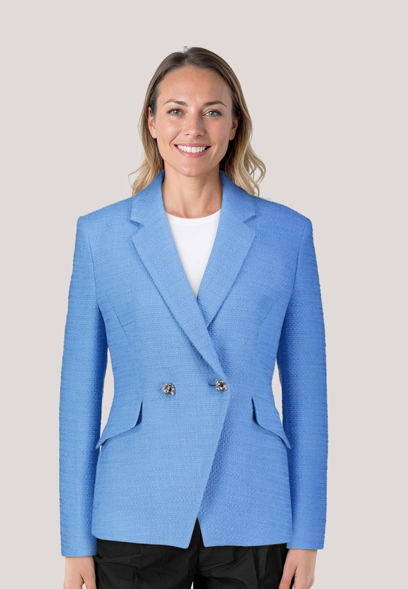 Blazer in Blau mit strukturiertem Stoff, doppelt geknöpftem Design, Reverskragen und silbernen Knöpfen. Kombiniert mit einem weißen Oberteil und einer schwarzen Hose.