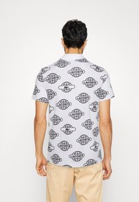 Kortärmad polo skjorta i ljusgrå bomull med ett upprepande mönster av svarta globar och Lacoste-logotyp, med klassisk krage och ren finish.