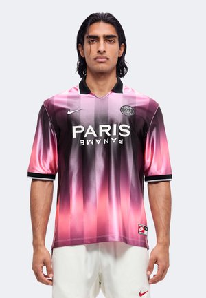 Junger Mann mit dunklem Haar trägt ein pink-schwarzes Paris Saint-Germain Nike Fußballtrikot mit vertikalen Streifen und weiße Shorts mit rotem Nike-Logo.