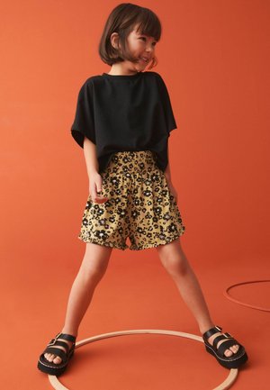 Svart oversized t-shirt med korta ärmar, kombinerad med gula leopardmönstrade shorts med smockad midja. Svarta platåsandaler.