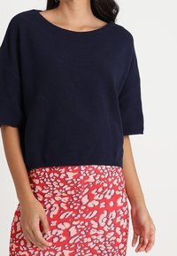 Mörkblå kortärmad stickad topp med vid halsringning, matchad med en livlig rosa kjol med ett vitt och blått abstrakt mönster.