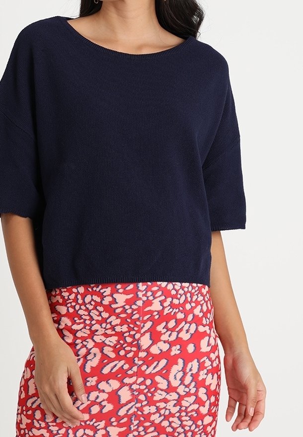 Mörkblå kortärmad stickad topp med vid halsringning, matchad med en livlig rosa kjol med ett vitt och blått abstrakt mönster.