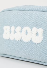Vaaleansininen denim-pussi, jossa on kohotettua valkoista froteekangasta teksti "BISOU." Muotoilu on suorakulmainen ja siinä on sileä pinta.