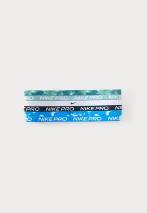 Cuatro cintas para la cabeza Nike Pro en camuflaje verde, blanco sólido, negro y camuflaje azul dispuestas horizontalmente sobre un fondo blanco.
