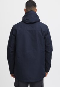 Marineblå hettegenser, laget av et teksturert, værbestandig materiale. Har en noe oversized passform med en rett nederkant og tette sømmer.