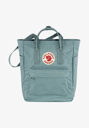Hellblaues Tote-Bag mit zwei Griffen oben, einer Vordertasche und einem runden Logo. Hergestellt aus strapazierfähigem Stoff mit einer glatten Textur.