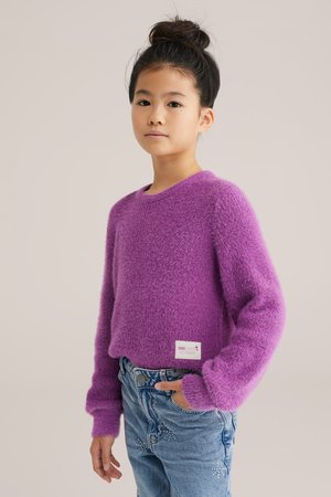 Purpurowy puszysty sweter z okrągłym dekoltem, długimi rękawami i ściągaczami. Zestawiony z niebieskimi spodniami o wysokim stanie z dekoracyjnymi akcentami.
