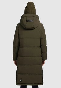 Olivengrøn pufferjakke med hætte, der har et quiltet design, elastiske manchetter og et logo patch på ryggen. Ribstrikket hue ovenpå.