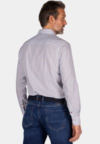 Witte blouse met lange mouwen en een klein rood en blauw bloemmotief, gestyled met donkere spijkerbroek en een zwarte riem, gezien vanuit de achterkant.