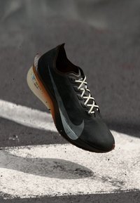 Schwarzer Nike-Laufschuh mit strukturiertem Obermaterial, weißen Schnüren und einem markanten silbernen Swoosh, der ein leichtes Design und eine orangene Sohle aufweist.