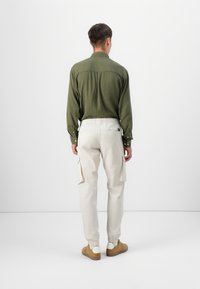 Green long-sleeve shirt with a textured fabric, paired with light beige cargo pants featuring side pockets and elastic cuffs. Brown shoes.