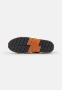 Rubber shoe sole with a textured black surface, featuring an orange midsole and a tan outer edge. Contains distinct tread patterns for traction.
