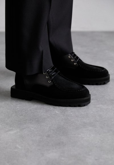 Scarpe nere che presentano una combinazione di camoscio e pelle liscia, con una suola in gomma spessa e dettagli di cucitura evidenti.