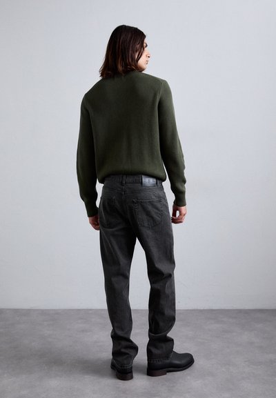 Green knit sweater, dark gray denim pants, black ankle boots. The outfit features a relaxed fit and textured fabric in a minimalist style.