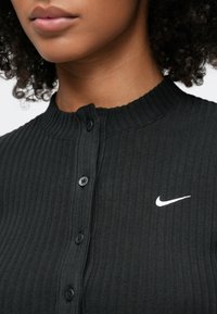 Μαύρο ριμπ τοπ με κουμπιά, ψηλό λαιμό, δύο μαύρα κουμπιά και λευκό λογότυπο Nike Swoosh στην αριστερή πλευρά.