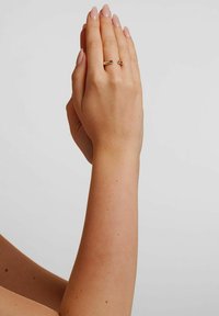 Gold ring with a thin band and a small gemstone, worn on a hand with neat, short nails, positioned in a clasped gesture.