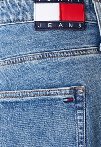 Denim jeans z lahkim modrim pranjem, z oranžnim šivom, zadnjim žepom s mali rdečim, belim in modrim zastavnim označevalcem ter značko logotipa.