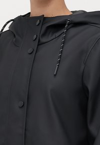 Zwart waterdicht jack met een hoge kraag, drukknopen aan de voorkant en een verstelbare capuchon met trekkoord en een gestructureerde afwerking.