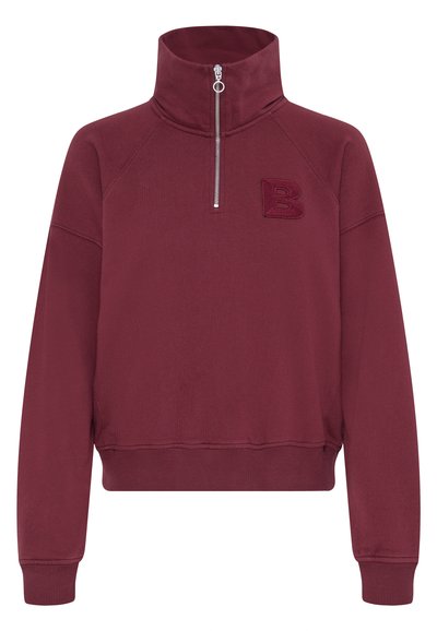 Burgundijas krāsas zip-up džemperis ar augstu apkakli, izšūta burts "B" un ribotām piedurknēm un apakšmalu, izgatavots no mīksta auduma ar gludu tekstūru.
