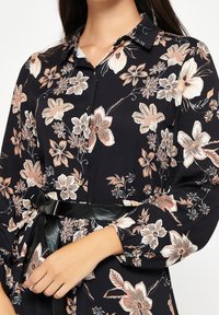 Vestido floral con base de tela negra y patrones florales en tonos durazno y blanco, con cuello abotonado y cinturón negro en la cintura.