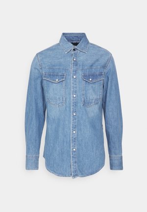 Šviesiai mėlyna džinsinė marškinė su ilgomis rankovėmis, apykakle, dviem krūtinės kišenėmis ir sagčių uždarymu. Suapvalintas apatinis kraštas ir kontrastingas siuvinėjimas.