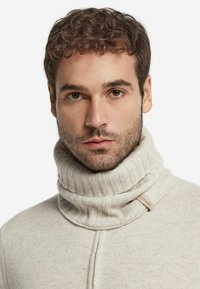 Lys beige strikket turtleneck sweater med ribbet tekstur og en fremtrædende krave. Har et lille stofmærke med teksten "CONERI."