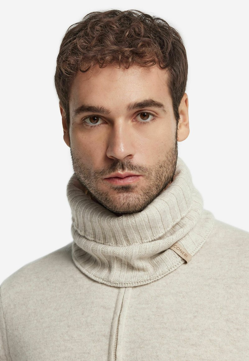 Lys beige strikket turtleneck sweater med ribbet tekstur og en fremtrædende krave. Har et lille stofmærke med teksten "CONERI."