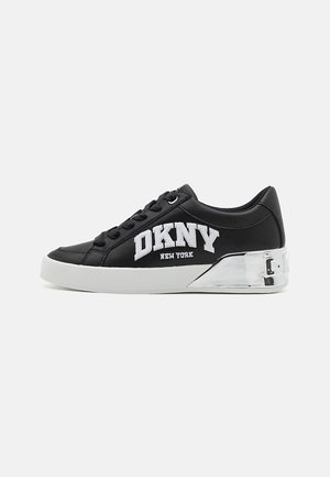 Baskets basses noires avec logo blanc "DKNY New York", lacets noirs, semelle blanche et détail talon argenté réfléchissant.