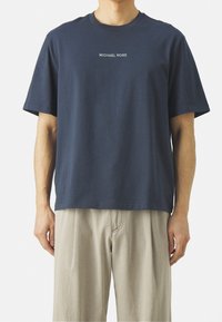 T-shirt in cotone blu navy con maniche corte, scollatura rotonda e testo bianco "MICHAEL KORS" centrato sul petto. Texture liscia.