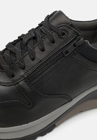 Schwarzer Lederschuh mit Mesh-Akzenten, runden Schnürsenkeln und einem seitlichen Reißverschluss. Merkmale eine graue Sohle mit strukturierten Details.