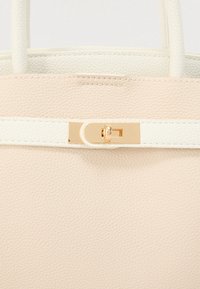 Sac cabas beige clair en similicuir texturé avec une bande accent blanche et une fermeture à loquet en métal doré.