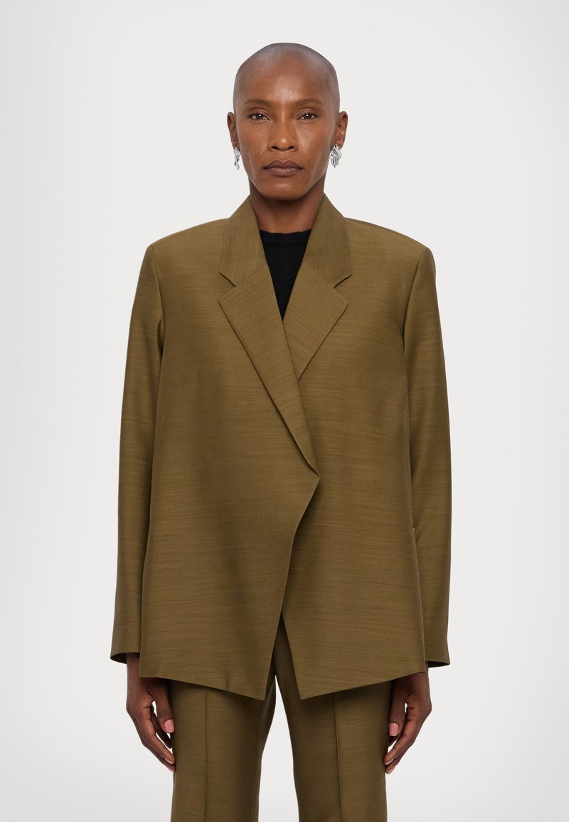 Sacou oversized de culoare verde măsliniu, cu rever clasic, fabrică texturată și croială dreaptă. Include mâneci lungi și tiv ușor evazat.