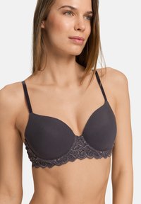 Tmavě šedá podprsenka s hladkými vycpanými košíčky, nastavovacími ramínky a krajkovým pásem s květinovým vzorem. Vyznačuje se zvlněným okrajem na spodním lemu.