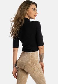 Top nero aderente con maniche corte abbinato a pantaloni beige chiaro a vita alta con motivo testurizzato e due tasche posteriori.