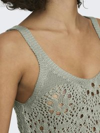 Ljusgrön stickad linne med öppen mönstring med stora och små hål, breda axelband och en texturerad yta.